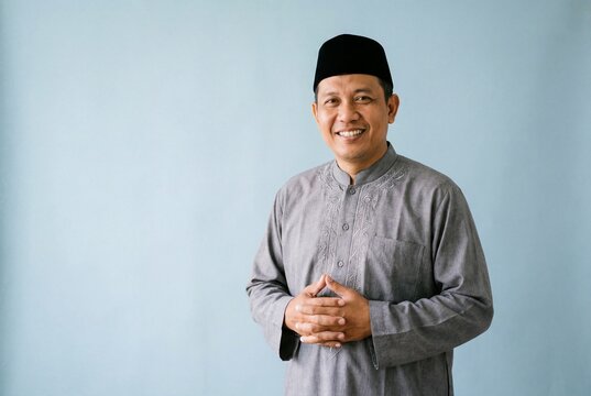 Smiling asian muslim man wearing a grey kurta and black songkok cap in a studio