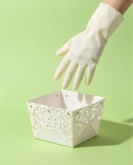 Hand Wearing Rubber Glove Over Decorative White Container on Soft Green Background