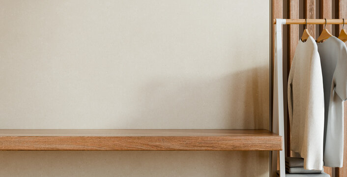 Empty wooden shelf and clothes rack with hanging t-shirts on beige wall background. Minimalist interior design mockup for product display and organization concept- 3D rendering