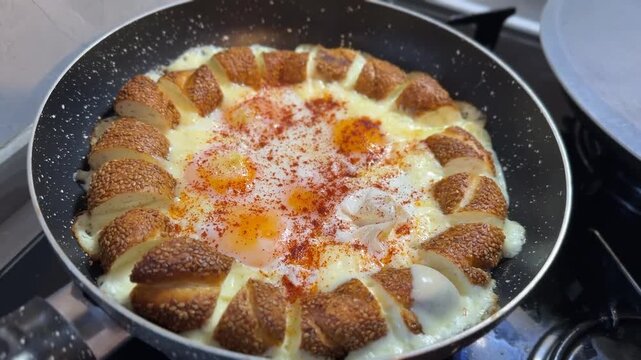 Turkish menemen cooked in frying pan with eggs, spices, and sesame bread, top view background