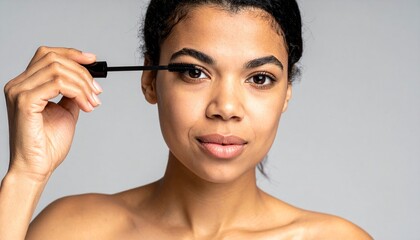 Fototapeta premium Beautiful Young African American Woman Applying Mascara for a Flawless and Radiant Look on Light Background.