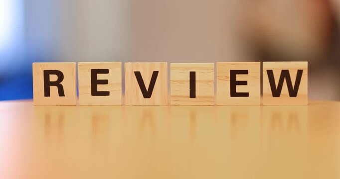 Wooden blocks spelling the word REVIEW arranged in a row on a reflective surface.