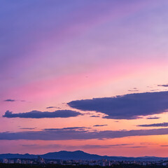 Obraz premium Breathtaking sunset sky with pink and purple hues over a distant city skyline and mountain range.