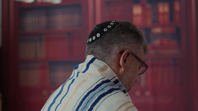 Men from the back, his head is covered by a traditional jewish kippah with blue and gold stripes and tassels. Close up view