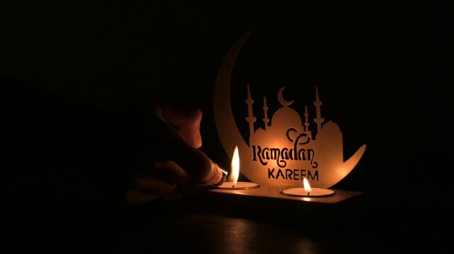 Hand lighting candles on Ramadan decor with mosque silhouette in dark ambience