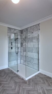 Modern bathroom featuring a walk in shower with glass screen, marble tiles, and herringbone pattern floor. vertical video