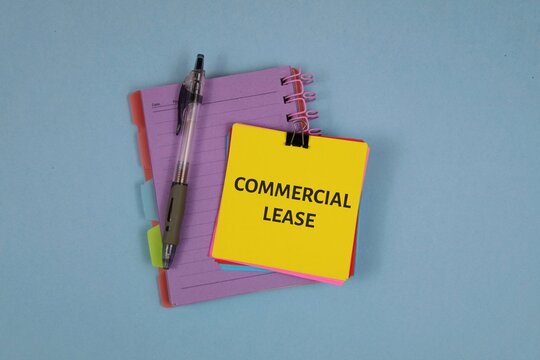 yellow sticky note reading 'COMMERCIAL LEASE' atop a purple notebook with a black pen, set against an blue background. Ideal for real estate, contracts, and office planning visuals.