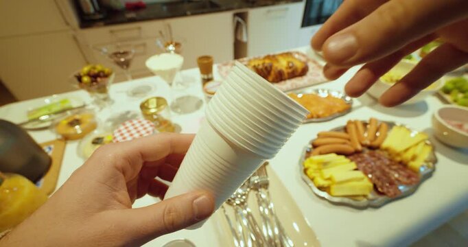 Practical stock footage showing a hand holding stacked plastic cups in front of a buffet table with food, symbolizing catering, events, self-service dining, convenience, and hospitality setup.