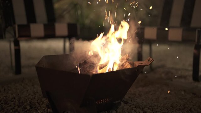 Fire pit burning logs creates a warm, inviting glow and sends sparks into the dark night, providing a cozy atmosphere for outdoor activities at a campground and cooking delicious marshmallows
