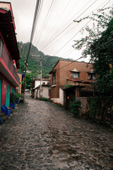 Pueblo mexicano con calle humedecida y empedrada con subida al cerro y casas con naturaleza en dia nublado de la monta&ntilde;a del tepozteco en tepoztlan morelos pueblo magico mexicano