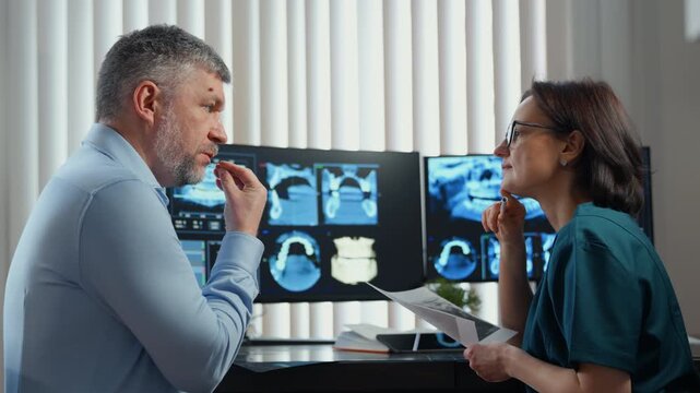 Dentist consulting patient while reviewing dental X-rays and scans on monitor, modern dental clinic diagnostics and oral healthcare.