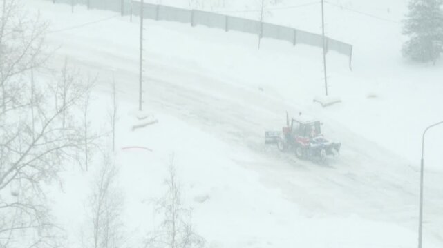 Snow removal tractor working on a city road during heavy snowfall, extreme winter weather, low visibility, road maintenance and urban transportation infrastructure concept