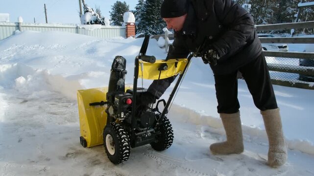 A man starts a petrol snowplow machine to clear the back yard of snow. Winter home maintenance and snow removal job in a suburban neighborhood.