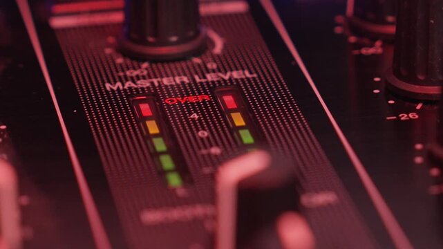 Close up of DJ mixer master meters hitting red, showing loud music audio overload in dark club setting