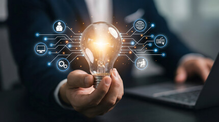 A professional hand holds a brightly glowing light bulb surrounded by interconnected digital technology icons in a modern office symbolizing innovatio