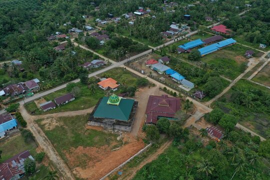 Aerial view of a central mosque with a prominent green roof in Karang Agung transmigration village, North Kalimantan, Indonesia. This shot captures the religious architecture and community planning in