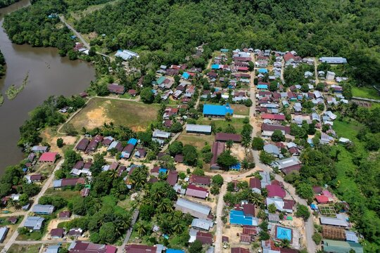 Panoramic aerial view of Kelincauan village in Sekatak, North Kalimantan, showcasing a community soccer field and residential housing along the winding Buji River. This drone perspective highlights th