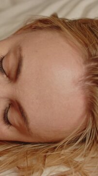 Stunning vertical close up of a blond woman lying in bed and moaning sensually in slow motion