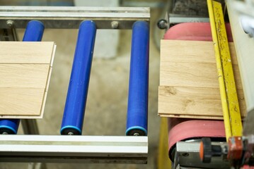 The process of sanding wooden boards on an industrial conveyor in a woodworking plant