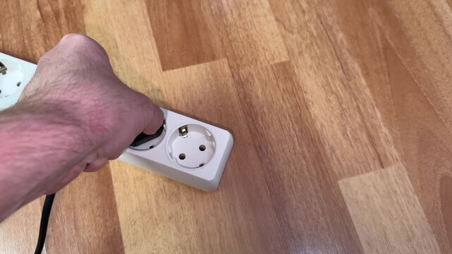 Extension cord on floor is electrocuted while plugging in device. Appliance is plugged into faulty surge protector. Person grabs plug and receives shock, safety concept