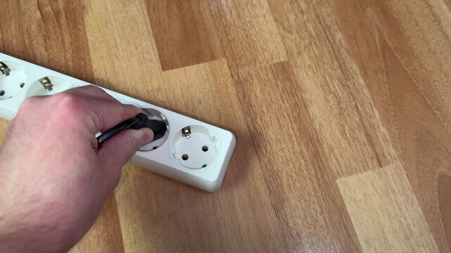 Hand grabs plug connected to surge protector, and person receives painful electric shock. Hand grasps cord in power outlet, conducting current throughout body. A hand shakes from electric shock