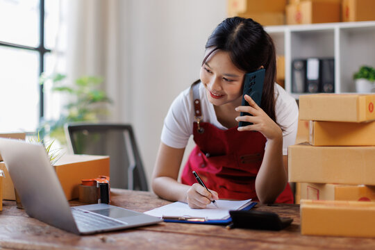 Asian woman small businesses SME owners asian female entrepreneurs call phone on receipt box and check online orders to prepare to pack the boxes, sell to customers, SME business ideas online.
