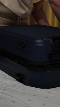 Women's hands close a suitcase lying on the bed of a hotel room or apartment