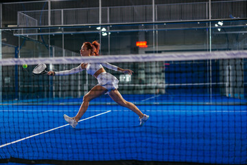 Two women play padel on a blue court, caught in the moment of a fast, athletic rally