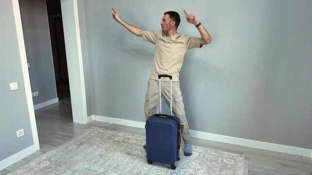 A cheerful and funny white man with a suitcase dances and celebrates, overjoyed at the prospect of his upcoming trip. Finally, he leaves the room to set off