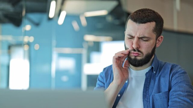 Man sitting in modern office experiences sharp toothache. Facial expressions convey discomfort and pain, interrupting work. Dental problem creates suffering while trying to focus on business.