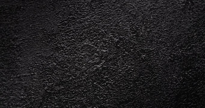 Macro Black Rough Texture Background. A seamless, slow panning footage across a deep black grainy surface revealing tactile depth through gentle shadow shifts and minimal highlights.