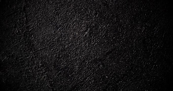 Macro Black Rough Texture Background. A seamless, slow panning footage across a deep black grainy surface revealing tactile depth through gentle shadow shifts and minimal highlights.