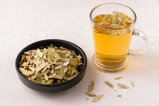 Clear glass cup of senna leaf tea with dried leaves on a black plate. A natural detox tea and traditional cleansing remedy with mild laxative effects