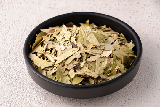 Dried senna leaves arranged on a black plate over a textured white background. A slimming herbal tea used for natural detoxification and body cleansing