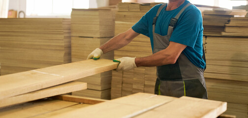 A worker processes wooden boards on a machine in a workshop.