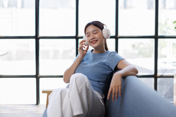 Fototapeta premium Young calm woman wear casual clothes listen music in headphones close eyes sit on armchair stay at home hotel flat rest relax spend free spare time in grey living room indoor. Lounge concept 