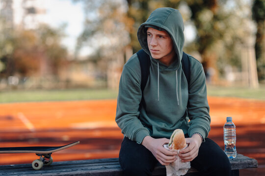 Teenage boy eating sandwich in park contemplating urban life