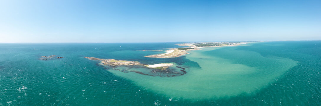 Wide aerial panorama of Pointe du Conguel and the islet of Toul Bihan, featuring turquoise and emerald waters, sandy stretches, and rocky outcrops under a clear blue sky. The scene is sunlit