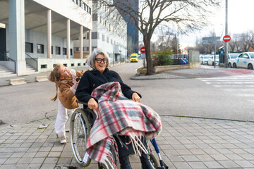 Obraz premium Granddaughter pushing smiling grandmother in wheelchair outdoors
