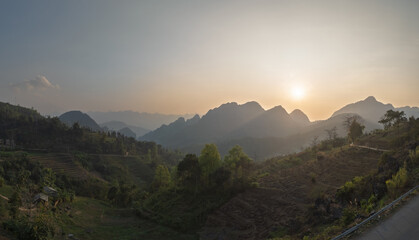 Sunset over terraced hills and karst peaks in warm golden light.