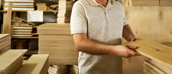 A man wearing gloves checks the quality of a wooden board in a carpentry workshop.