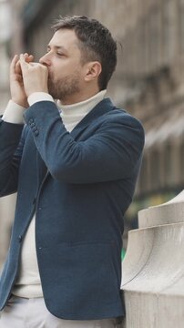 A man in a blue jacket plays the harmonica on the street during the rain