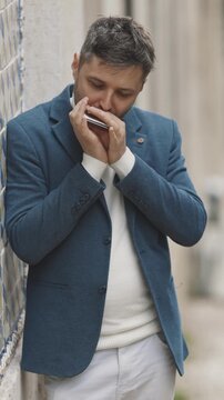 A man stands by a wall on the street and plays the harmonica