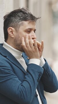 A man stands against the wall and plays the harmonica in the street
