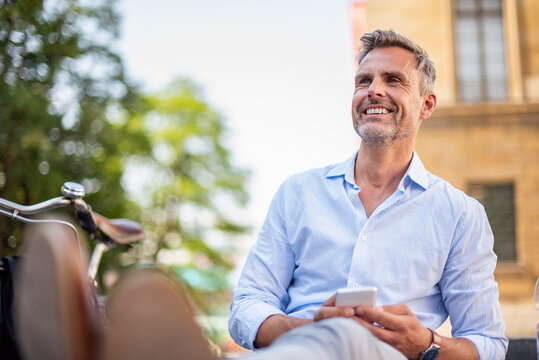 Businessman taking a break with bicycle and smartphone in city