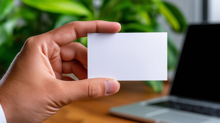 Obraz premium A hand offering a blank textured linen business card against a blurred modern office backdrop.