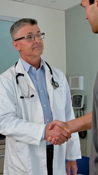 Mature doctor shaking hands with a male patient during a medical consultation in a clinic, vertical shot