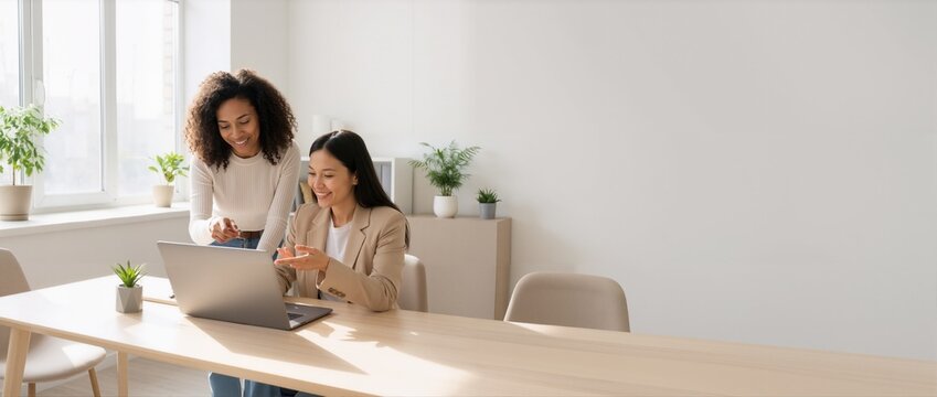 Two diverse women collaborating on a laptop in a bright modern office space.