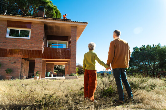 Couple holding hands in garden looking at house on sunny day