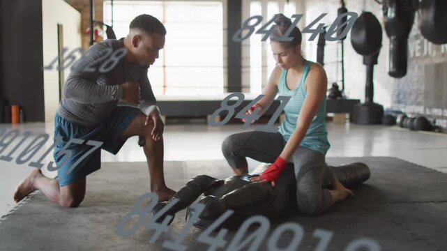 Coach gesturing, trainee practicing boxing technique on bag, numeric graphics appearing over gym